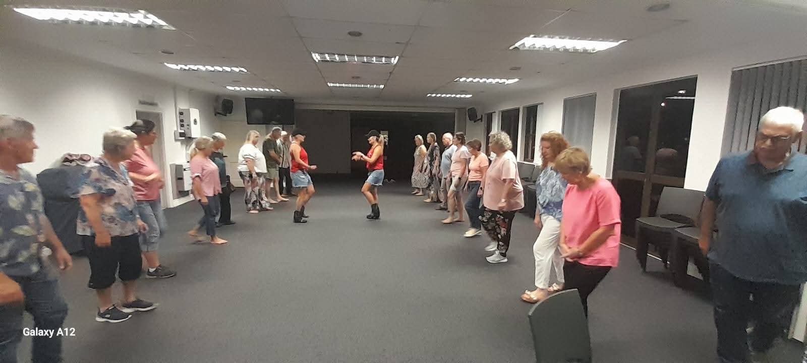 A group practising line dancing in two rows during an indoor evening class