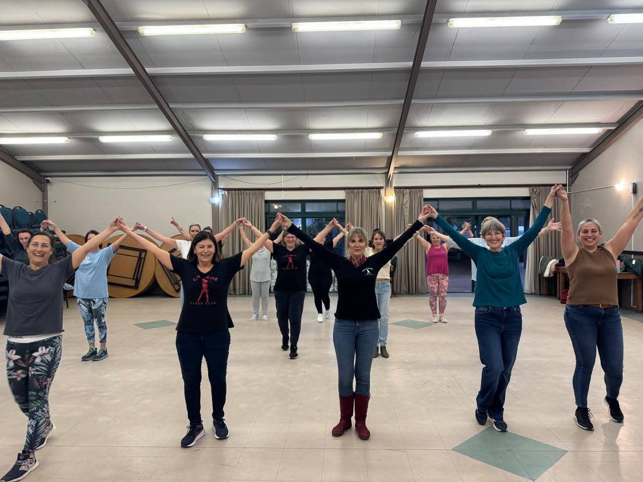 Dancers smiling with joined hands raised during a Line & Wine class
