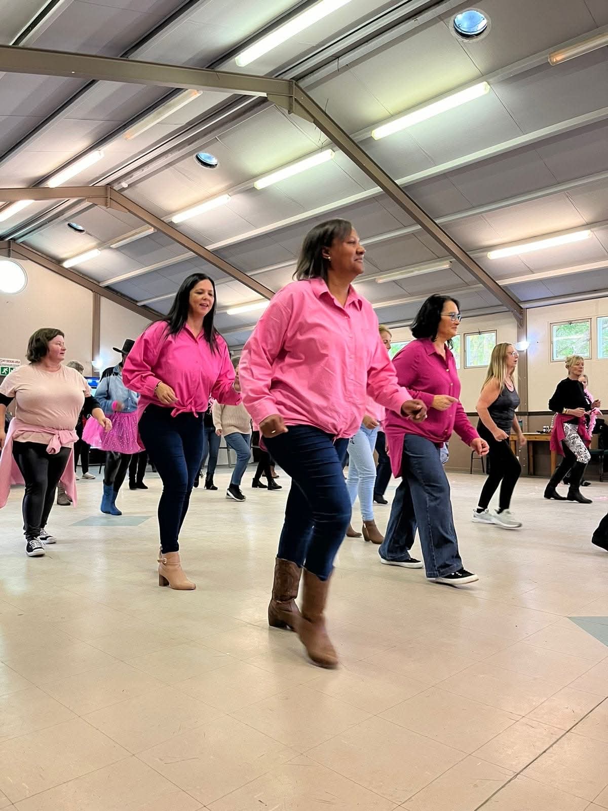 Dancers in pink shirts practising line dancing in a community hall