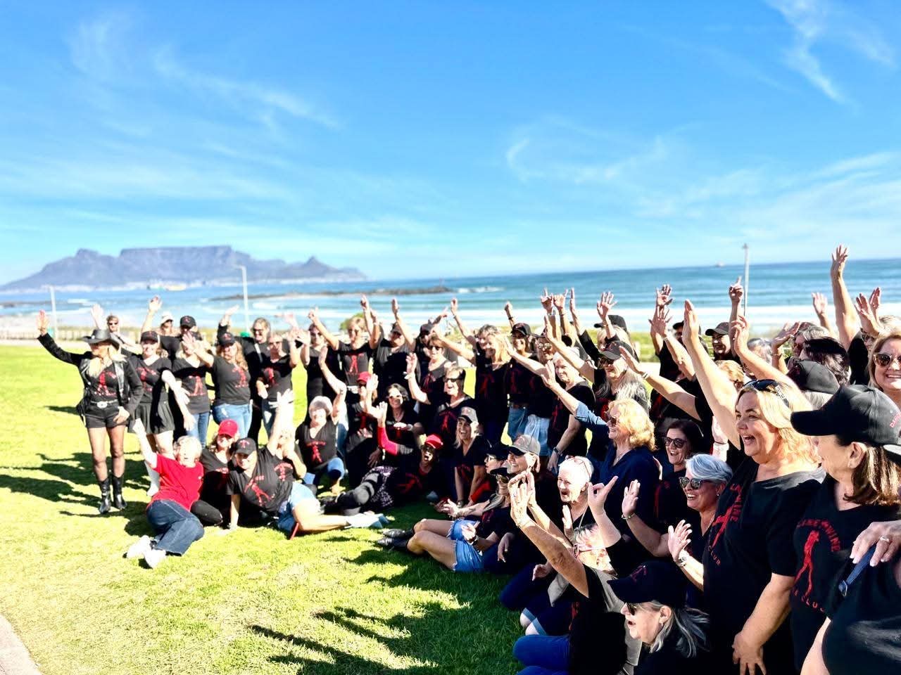 Line & Wine members celebrating on the grass beside the sea with Table Mountain behind them